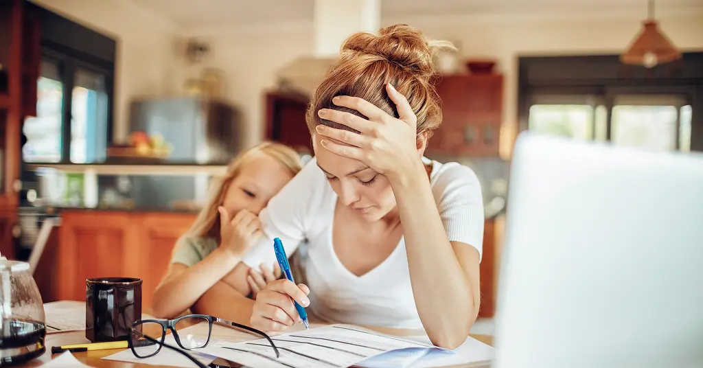 Mutter sitzt gestresst am Küchentisch über Unterlagen – berufliche Neuorientierung und Berufsorientierung für Mütter in Berlin.