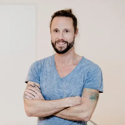 Mann mit Bart und Dutt lächelt selbstbewusst mit verschränkten Armen – Akademiker Coaching Berlin für Neuorientierung und Wiedereinstieg