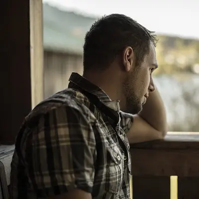 Nachdenklicher Mann blickt aus dem Fenster, Symbolbild für Belastung und Orientierungssuche.