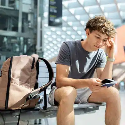 Ein Junger Mann mit braunen, kurzen Locken sitzt mit einem Smartphone auf einer Bank und überlegt, in welche Richtung es jetzt gehen soll.