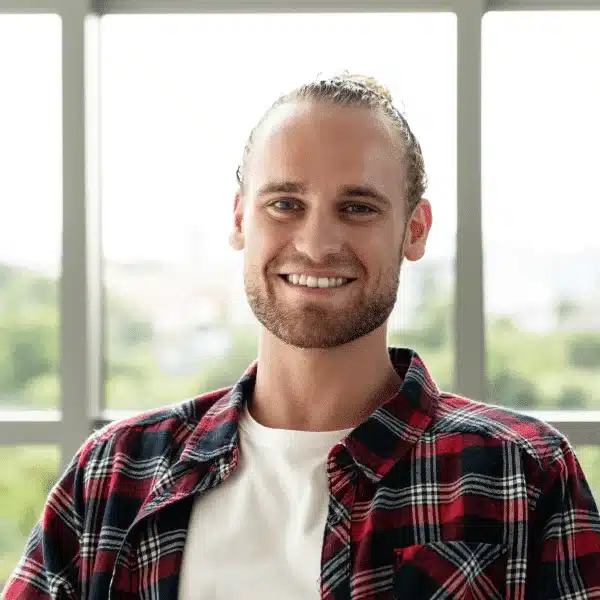 Ein lächelnder Mann mit Bart trägt und einem kariertes Hemd, beim AVGS Coaching Berlin. Die Arbeitsumgebung ist hell und freundlich.