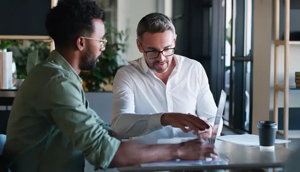 Zwei Männer im Gespräch am Laptop im Büro, während eines Bewerbungscoachings in Berlin