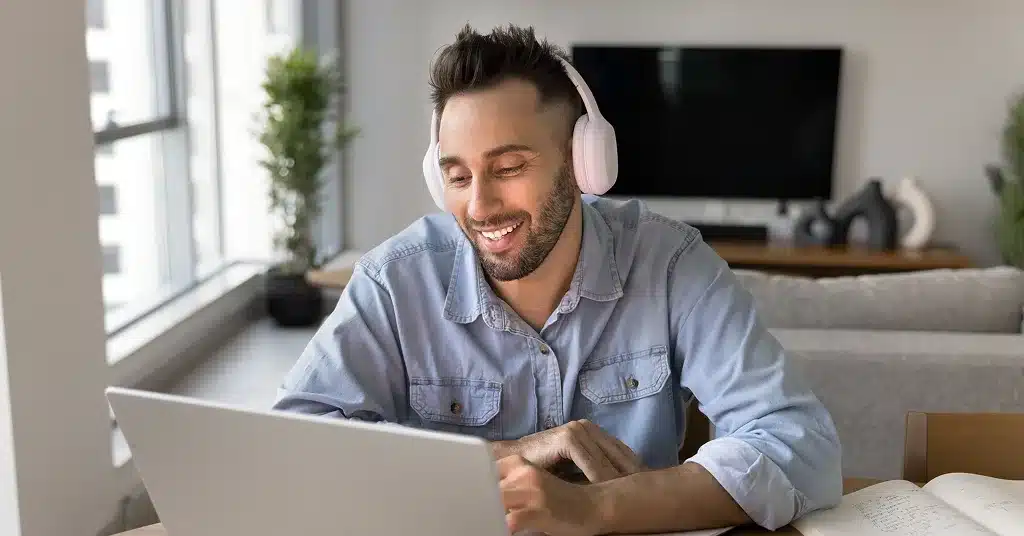 Internationale Fachkraft nimmt lächelnd an einem AVGS Coaching auf Englisch in Berlin teil – Online-Coaching-Sitzung am Laptop mit Kopfhörern